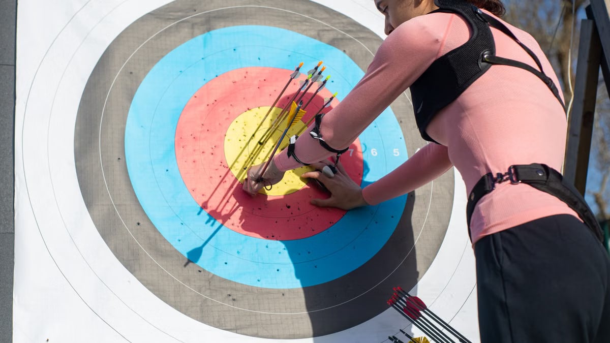 A female archer inspects arrows on a target after a shooting session outdoors.